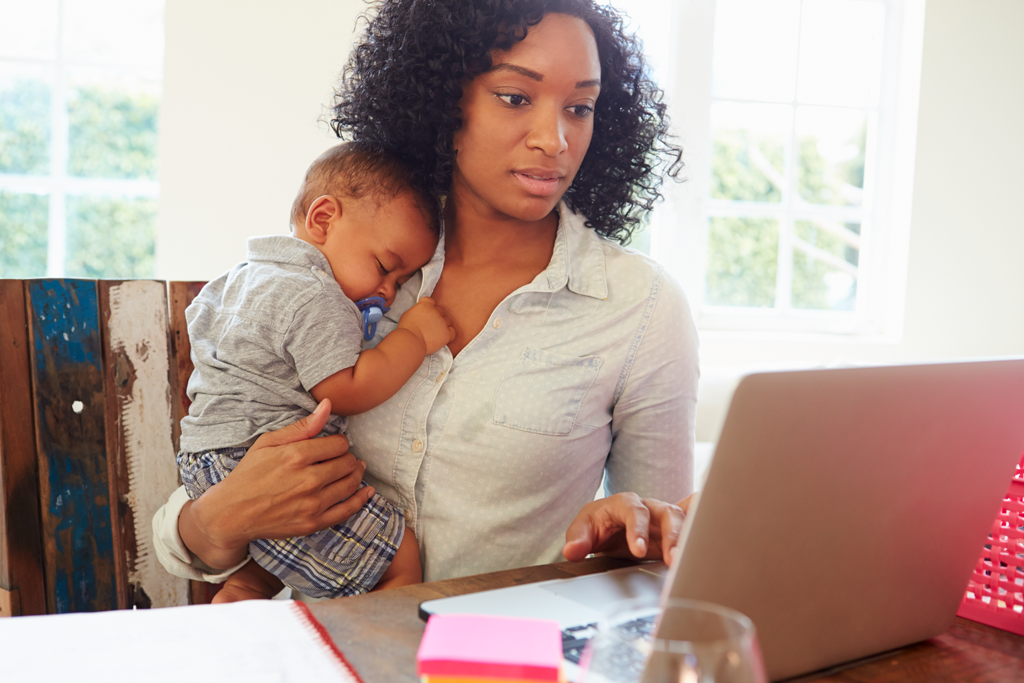 Woman working on laptop with newborn baby