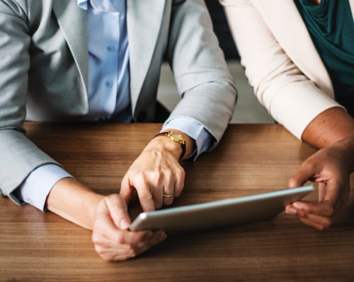 pexels-adult-banking-blonde-1059119 Two sets of hands on a tablet over a wooden table.