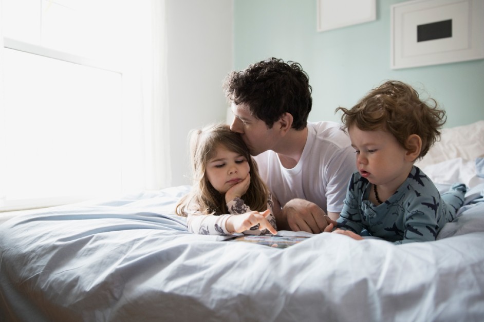 A young father playing in bed with his young children in their pajamas
