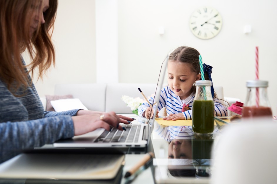 A mother and young daughter sitting at the kithen table busy with their work.