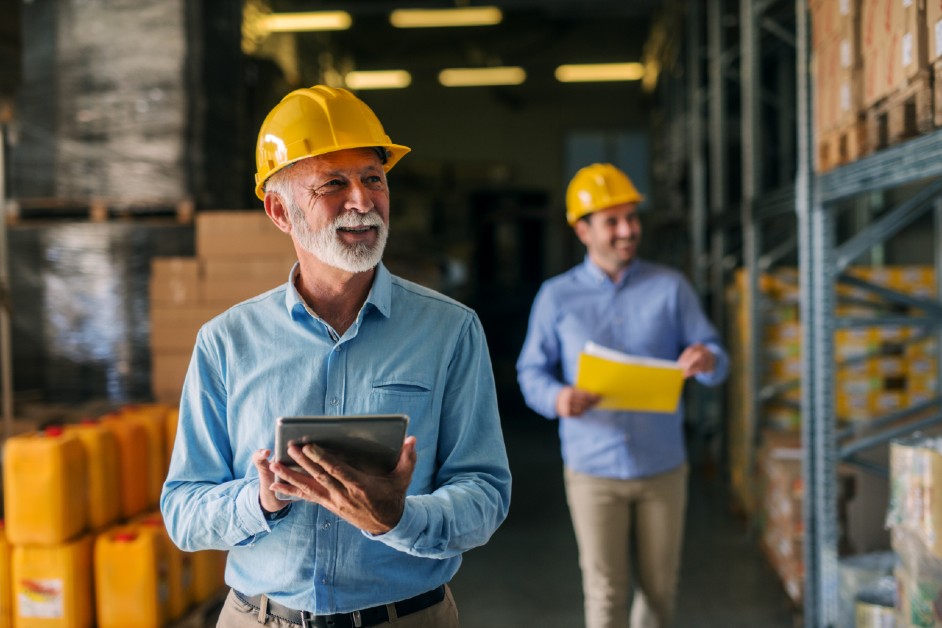 Two workers wearing hard hats taking stock in a warehouse.