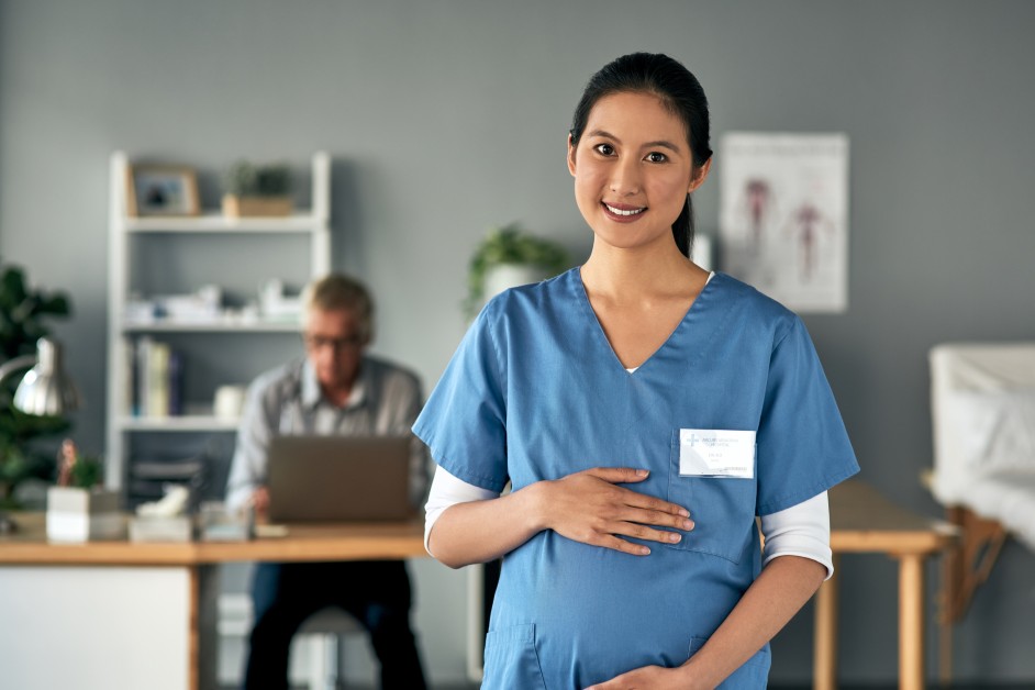 A pregnant employee cradles her baby bump in an office setting