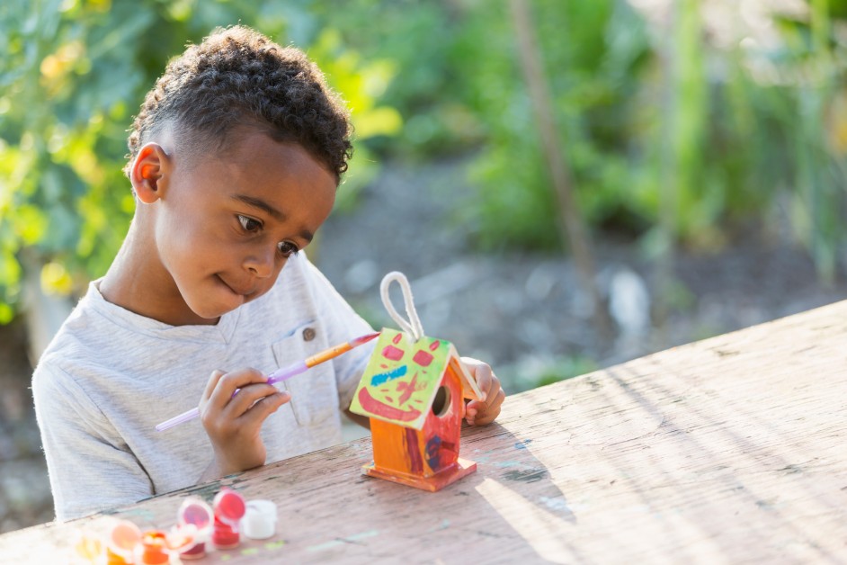 A young black child painting a tiny model of a house