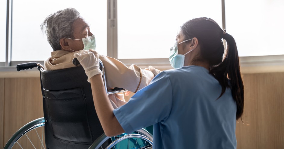 Nurse helping man in wheelchair during a pandemic