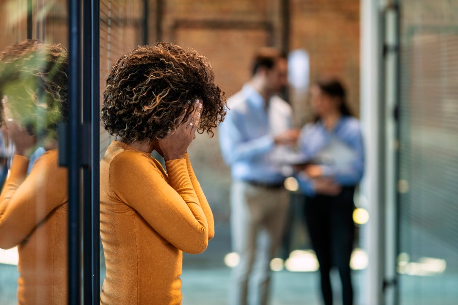 Woman upset at work while coworkers chat behind her